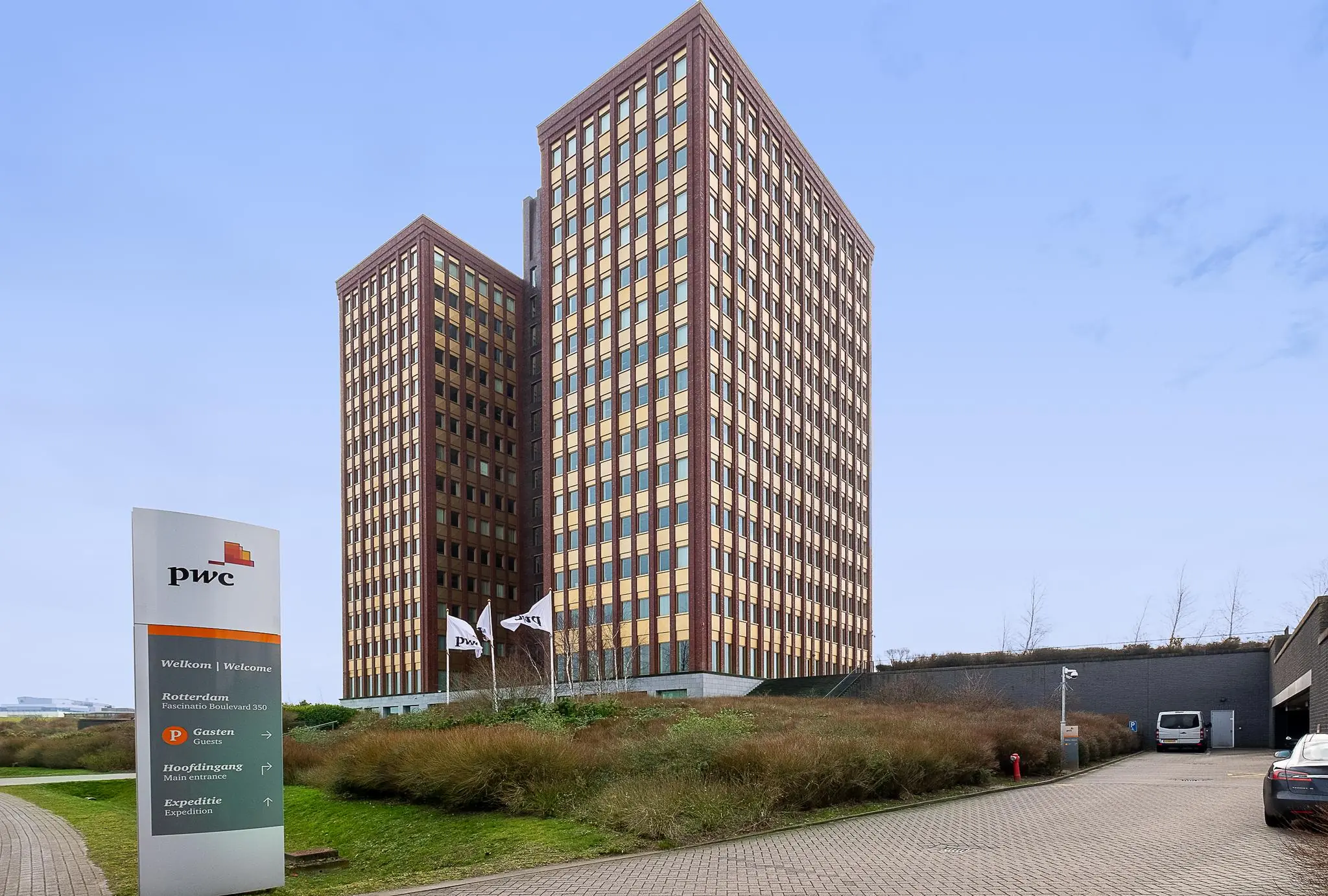 Twee hoge kantoorgebouwen van PwC aan de Fascinatio Boulevard in Rotterdam met vlaggen en bewegwijzering op de voorgrond.